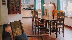 A dining area with a round wooden table and chairs, a cabinet with glass doors, and a window with curtains. - Family-friendly vacation home - 300m to the sea (Wurster Nordseeküste)