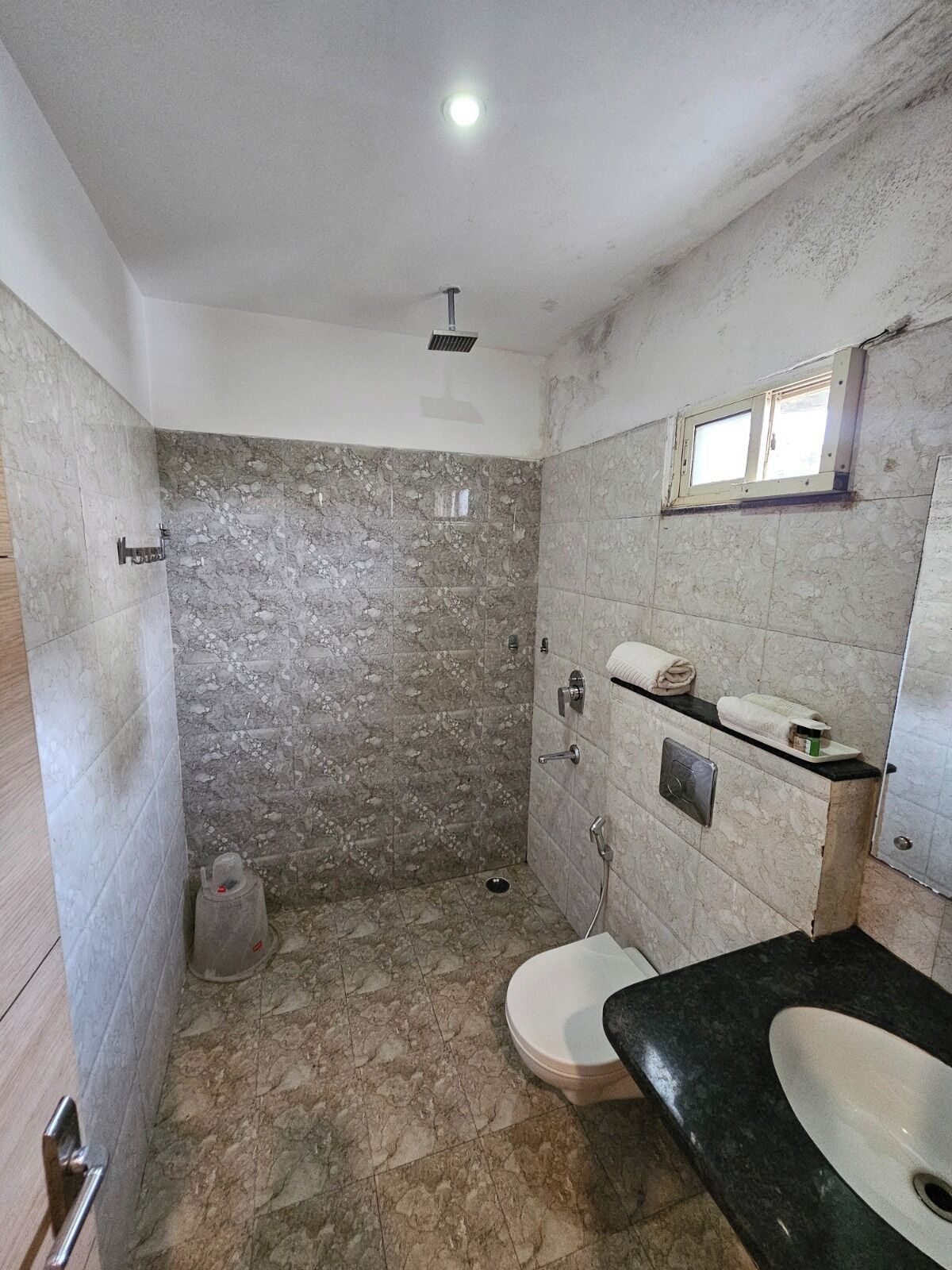 A bathroom with a shower, toilet, and sink, featuring marble walls and a black countertop.