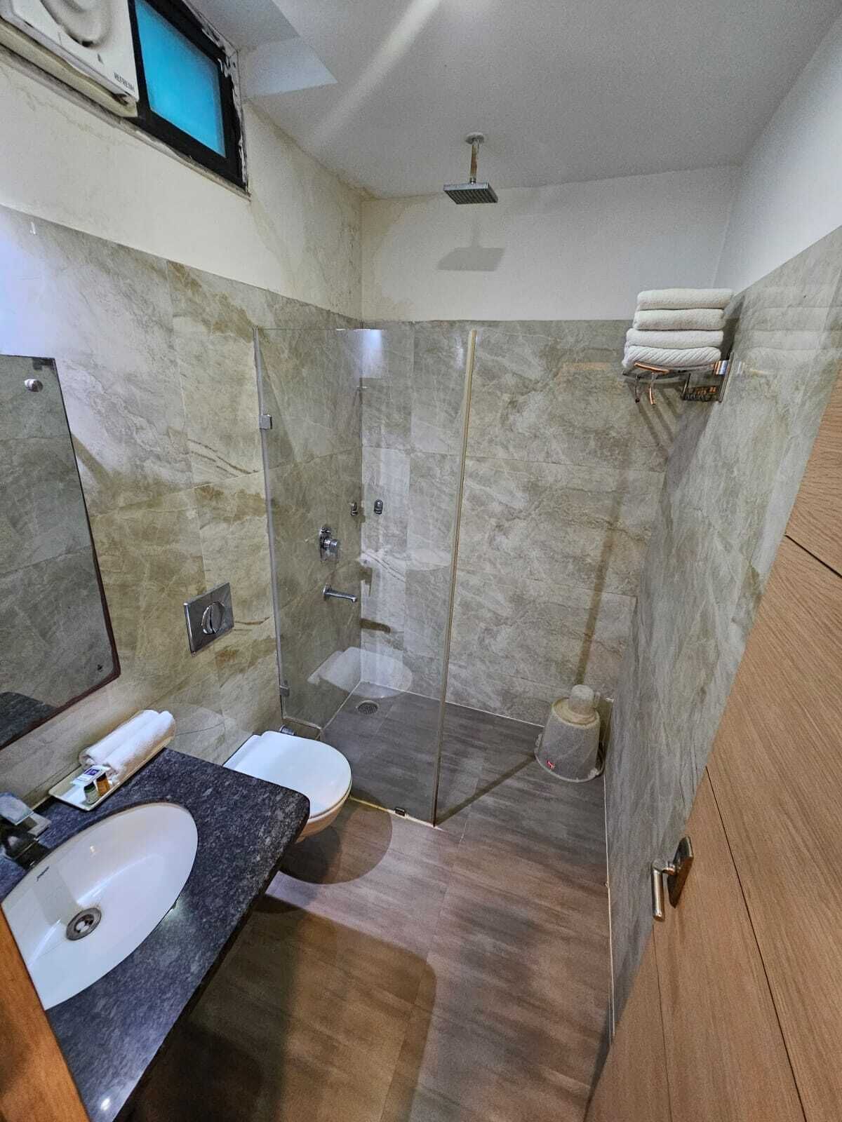 A bathroom with a marble shower, a sink, and a toilet.