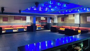 Un espacio lounge moderno con asientos rojos, una mesa larga e iluminación ambiental azul.