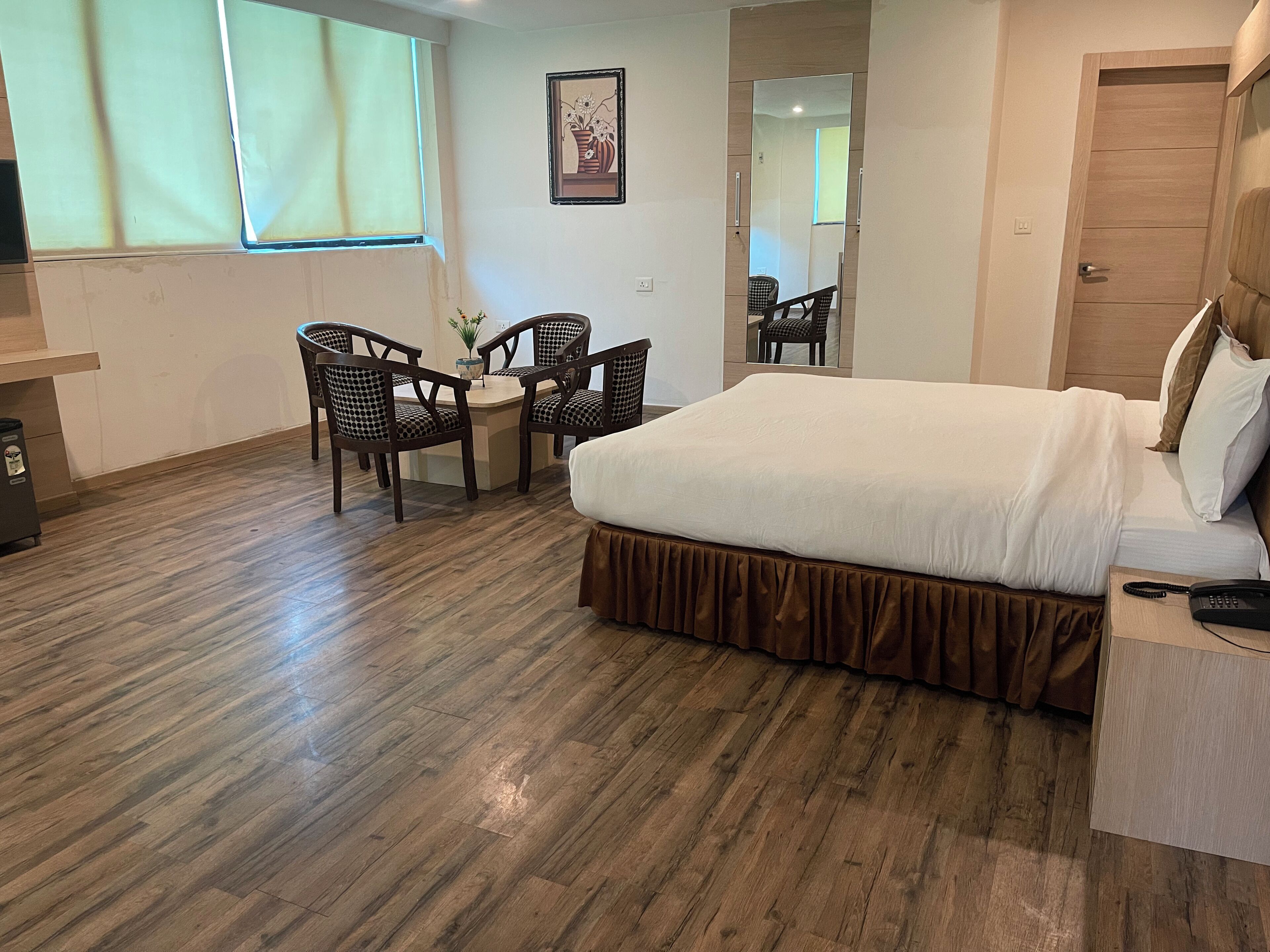 A hotel room with a bed, two chairs, a small table, a mirror, and a window.
