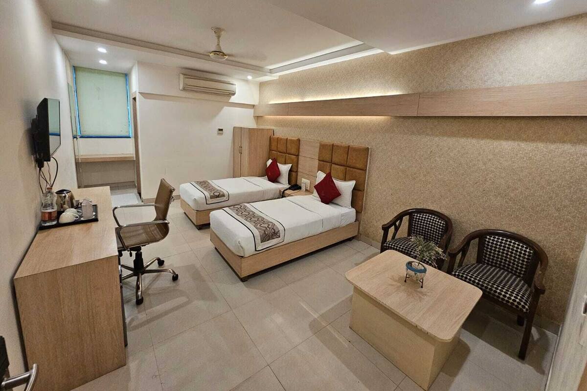 A hotel room with two beds, a desk, a chair, and a TV.