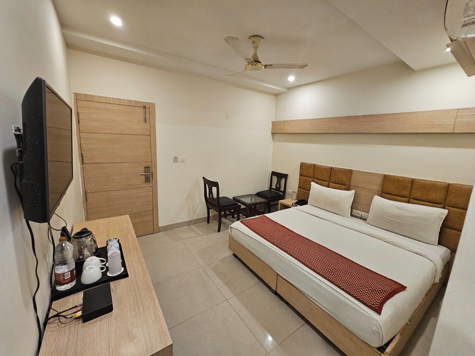 Una habitación de hotel con cama, escritorio, televisor, silla y ventilador de techo.
