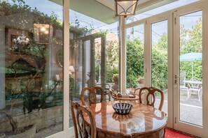 A dining area with a round table, chairs, and a glass partition with a view of greenery and a fountain. - Apartment 'Manuela' with Shared Pool, Wi-Fi and Air Conditioning (Marginone)