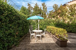 A patio with a table and chairs, an umbrella, and a planter with plants.