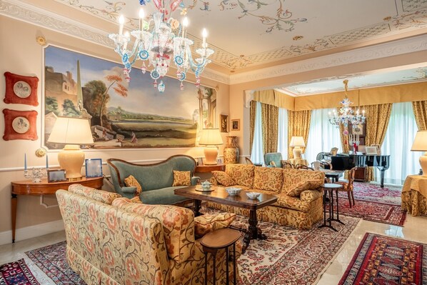 A spacious living room with a large painting, a chandelier, and a piano.