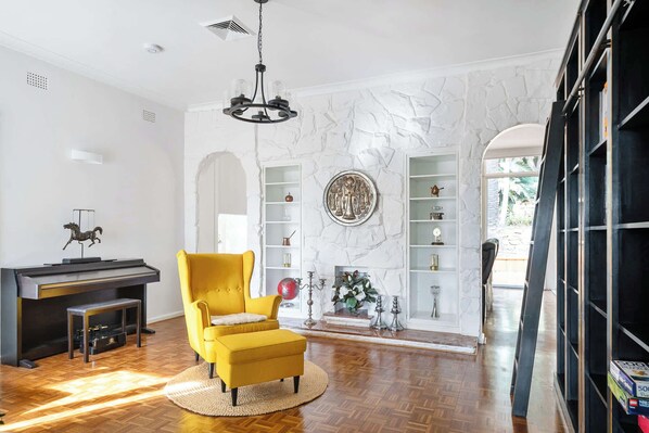 A living room with a piano, a yellow armchair, a fireplace, and a bookshelf.