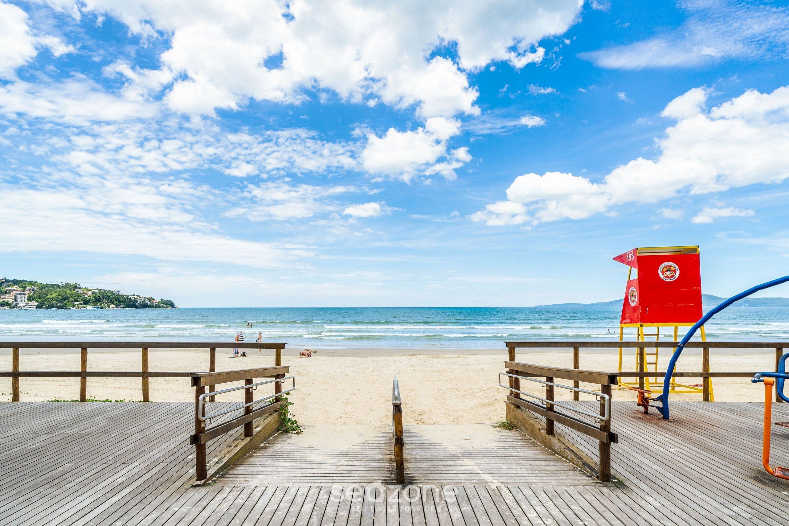 A wooden boardwalk leading to a beach with a lifeguard tower.