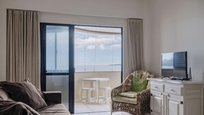 Un salon comprenant un canapé, un téléviseur posé sur un meuble, un fauteuil et un balcon avec une table et des chaises.