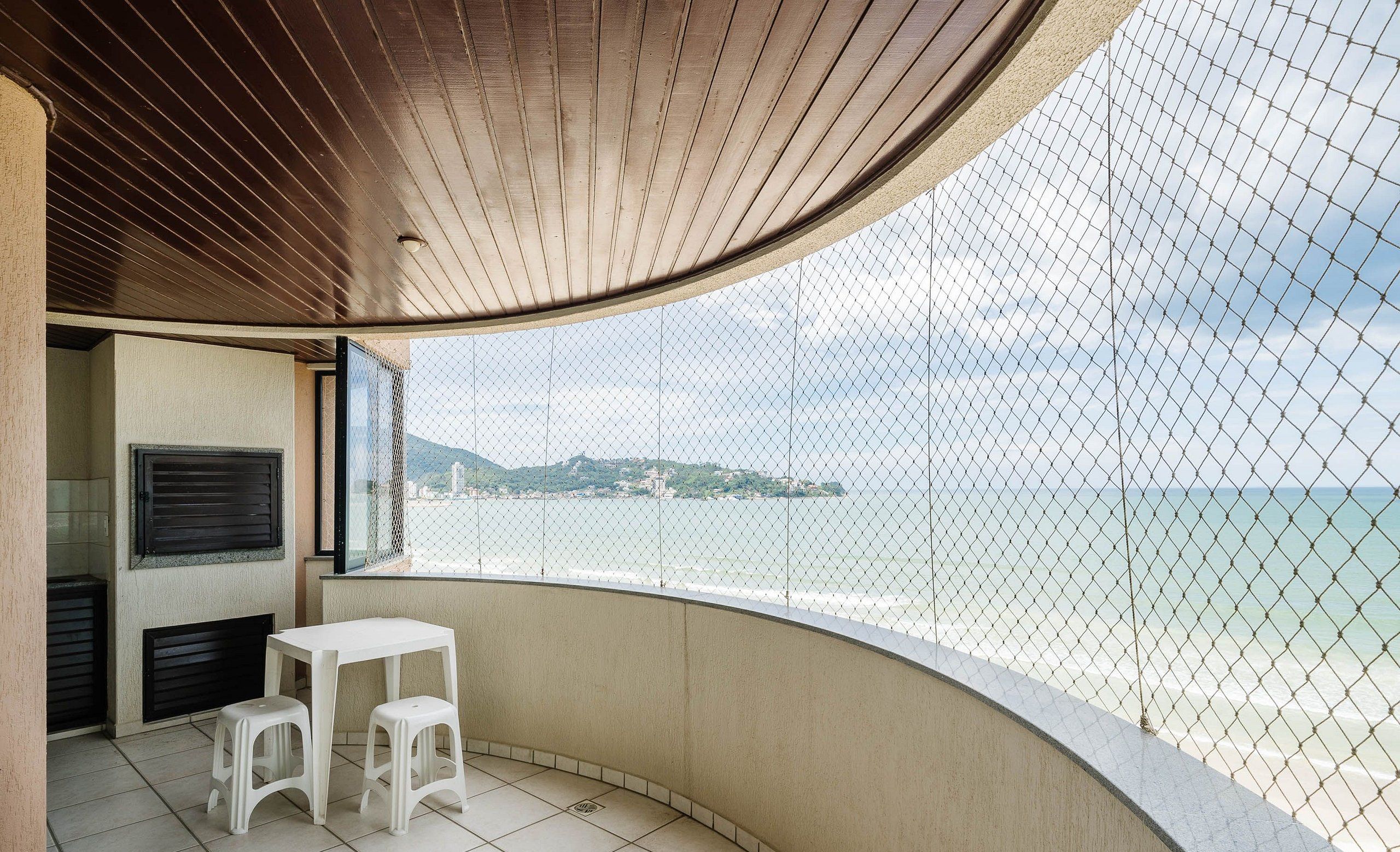 A balcony with a white table and stools, a view of the sea, and a wooden ceiling.