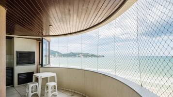 A balcony with a white table and stools, a view of the sea, and a wooden ceiling.