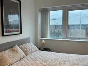 A bedroom with a bed, a nightstand, a lamp, a window with curtains, and a framed picture on the wall.