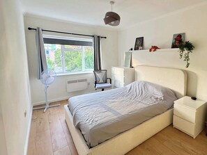 Une chambre à coucher comprenant un lit, un bureau, une chaise, un radiateur et une fenêtre avec des rideaux.
