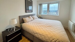 A bedroom with a bed, a bedside table, a lamp, a window, and a picture on the wall.