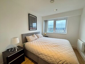 A bedroom with a bed, a bedside table, a lamp, a window, and a picture on the wall.