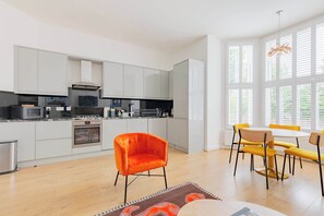 A modern kitchen with white cabinets, a microwave, stove, and a dining area with yellow chairs and a table.