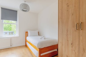 Un dormitorio con cama de madera, un radiador, una ventana con persiana y un armario de madera.