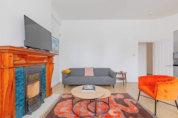 Una sala de estar con chimenea, sofá, mesa de centro y un sillón naranja.