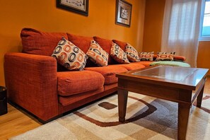 A living room with a sofa, patterned cushions, a glass-top coffee table, and a rug.