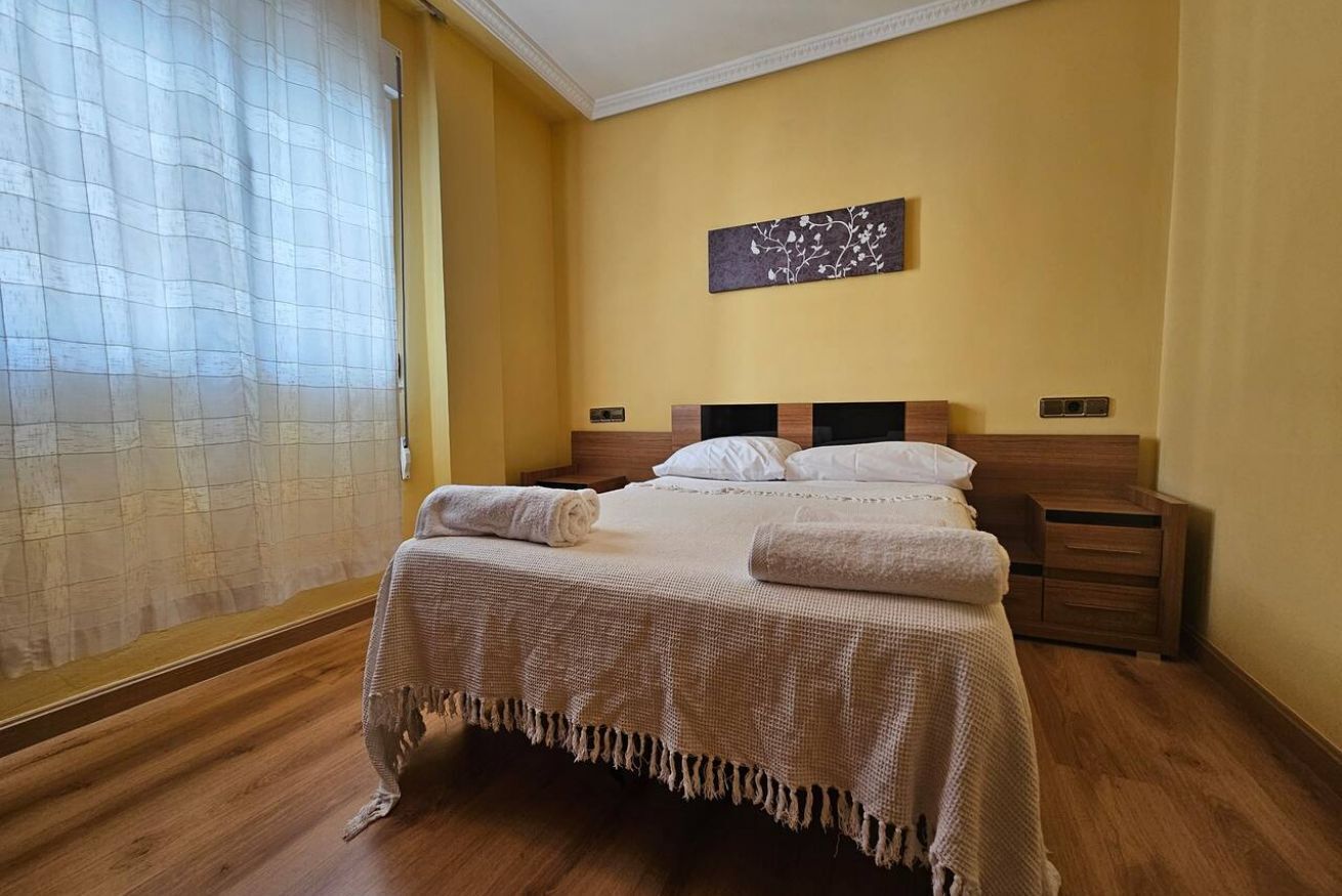 Un dormitorio con cama, mesitas de noche, una obra de arte en la pared y una ventana con cortinas.