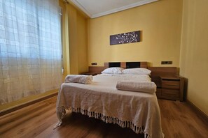 A bedroom with a bed, bedside tables, a wall-mounted artwork, and a window with curtains.