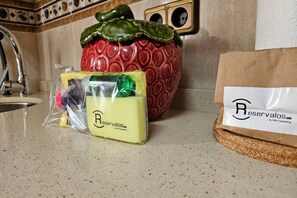 A kitchen counter with a red fruit-shaped container, a plastic bag with a logo, and a paper bag with a logo.