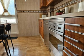 A kitchen with wooden cabinets, a stainless steel oven, and a window with curtains.