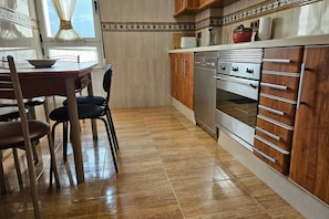 A kitchen with a dining table, chairs, a refrigerator, an oven, and wooden cabinets.