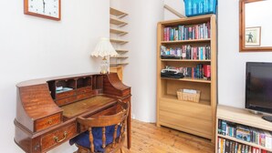 A room with a wooden desk, a bookshelf, a lamp, and a television.