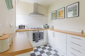A kitchen with white cabinets, a microwave, a stove, and a checkered floor. There are framed pictures on the wall.