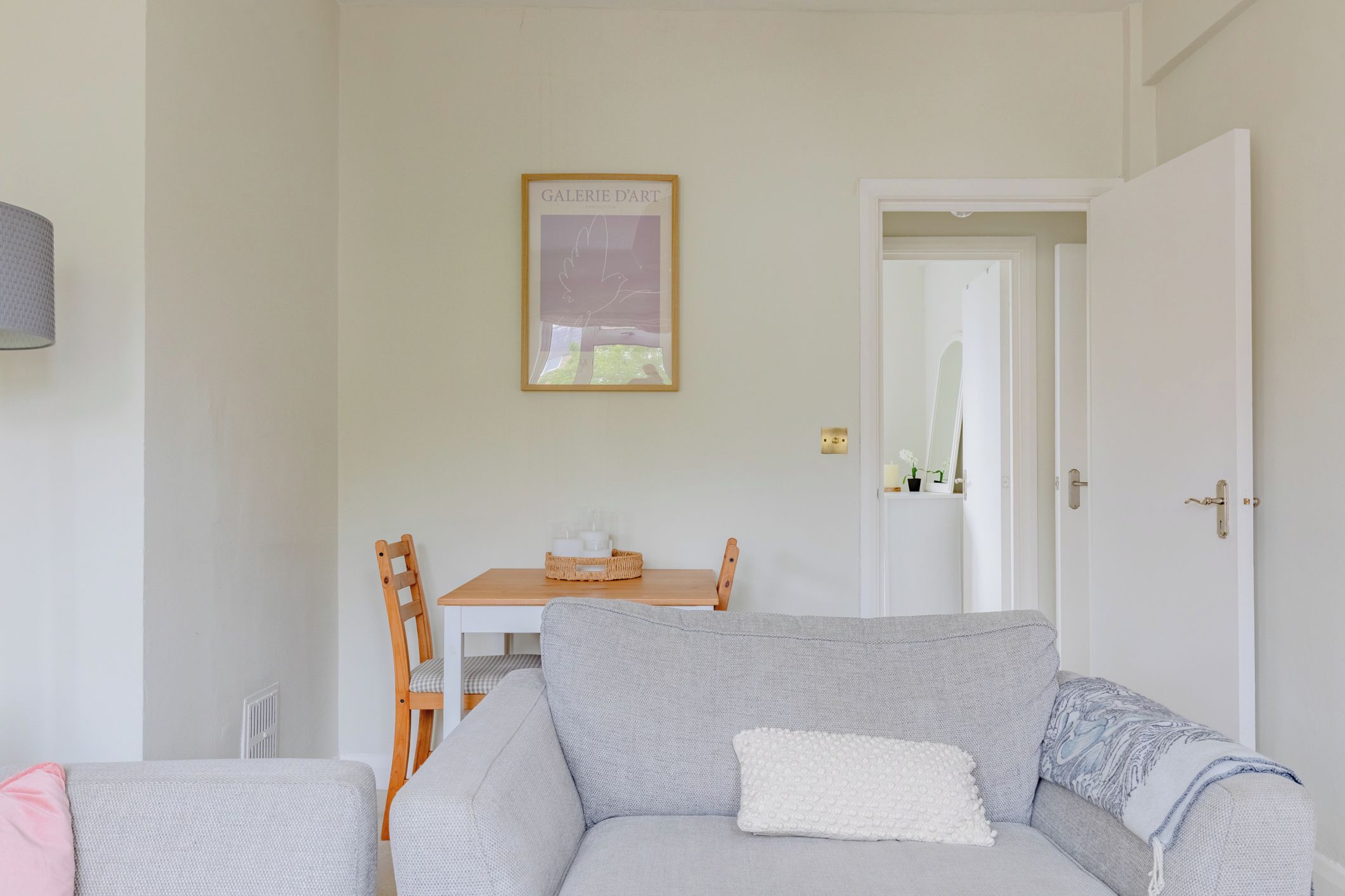 Un salon avec un canapé gris, une petite table sur laquelle se trouve un panier, et un tableau encadré accroché au mur.