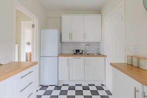 A compact kitchen with white cabinets, a black and white checkered floor, and a refrigerator.