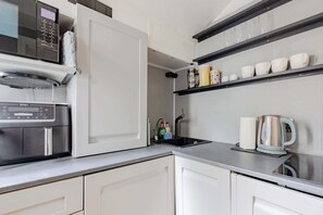 Een keuken met een magnetron, waterkoker en planken met kopjes.