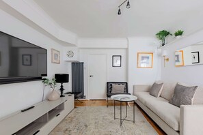 A modern living room with a flat-screen TV, a sofa, a coffee table, and a radiator. - Contemporary 1BD Flat in Unbeatable City Location (Greater London)