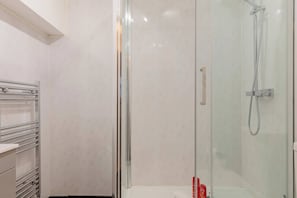 A glass-enclosed shower with a handheld showerhead, a towel rack, and a white tiled wall. - Contemporary 1BD Flat in Unbeatable City Location (Greater London)