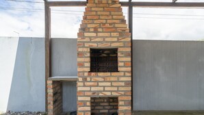 A brick-built outdoor fireplace with a metal grate, set against a concrete wall. - 3BR Home w/ BBQ 100m From Beach Rpr056 (Penha)
