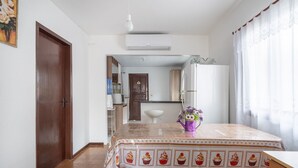 A dining area with a table covered in a cupcake-patterned tablecloth, a purple watering can with flowers, and a white air conditioning unit above. - 3BR Home w/ BBQ 100m From Beach Rpr056 (Penha)