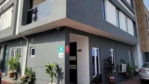 Un immeuble moderne à plusieurs étages, doté de balcons, de plantes en pot et d’un espace d’entrée pavé.