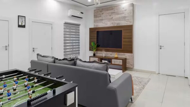 Un salon moderne avec un baby-foot, des canapés gris, un téléviseur à écran plat et un mur d’accent en bois.