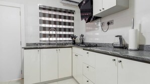 Une cuisine moderne avec des meubles blancs, un plan de travail en marbre, une fenêtre avec des stores, un climatiseur et une machine à café.
