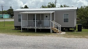 A single-story mobile home with a porch, a small front yard, and a gravel driveway. - Cozy camp on private property minutes from hunting, fishing and restaurants. (Buras)