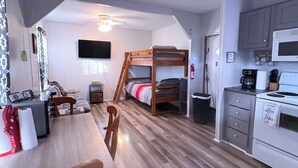 A compact room with a bunk bed, a dining table with chairs, a kitchen area with a microwave, and a flat-screen TV mounted on the wall. - Cozy camp on private property minutes from hunting, fishing and restaurants. (Buras)