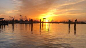 A calm waterfront at sunset with boats and dock structures. - Cozy camp on private property minutes from hunting, fishing and restaurants. (Buras)