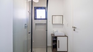 A modern bathroom with a glass shower enclosure, a small window, a white sink, and a wooden cabinet. - Apto 2Q c/ churrasq. 500m da Meia Praia ROT1001 (Itapema)