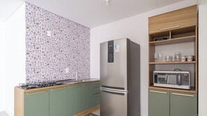 A modern kitchen with green cabinets, a stainless steel refrigerator, and a microwave on a wooden shelf. - Apto 2Q c/ churrasq. 500m da Meia Praia ROT1001 (Itapema)