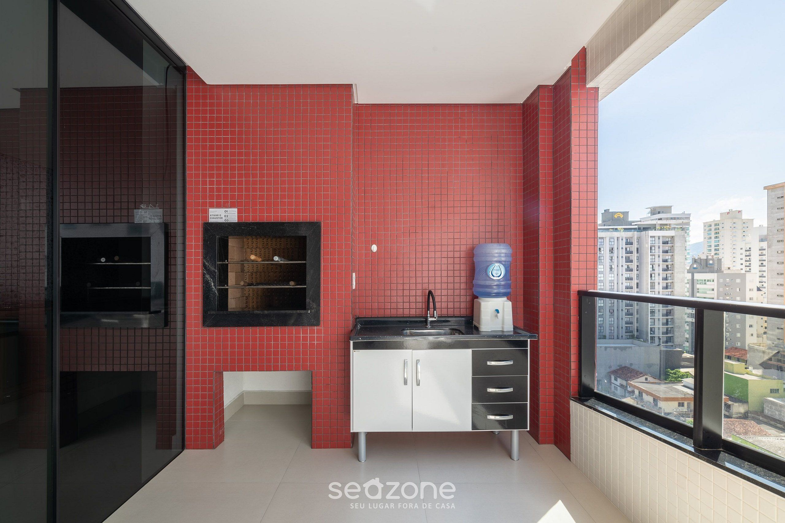 A modern kitchen with red tiles, a water dispenser, and a view of the city.