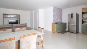 A modern kitchen with a dining area, a built-in TV, and a refrigerator. - Apto 2Q c/ churrasq. 500m da Meia Praia ROT1001 (Itapema)