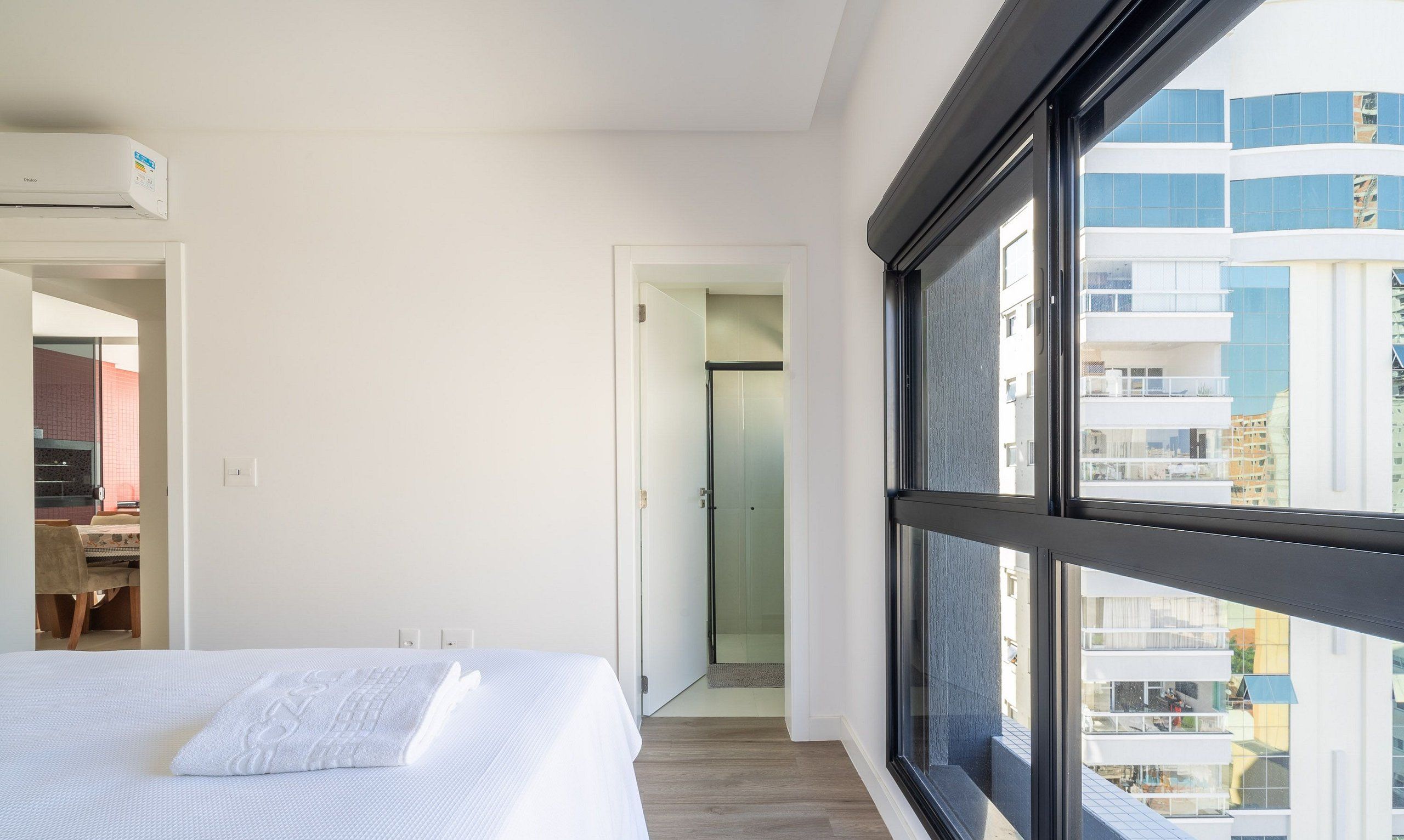 Une chambre d’hôtel moderne dotée d’une grande fenêtre, d’un lit, d’un bureau et d’un espace douche.