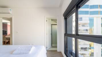 Une chambre d’hôtel moderne dotée d’une grande fenêtre, d’un lit, d’un bureau et d’un espace douche.