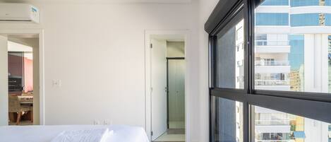 A modern hotel room with a large window, a bed, a desk, and a shower area.